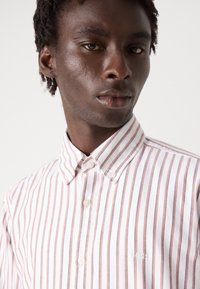 Camicia bianca con bottoni, decorata con righe verticali rosse e grigie. Presenta un colletto classico e il logo "BOSS" ricamato sul petto.
