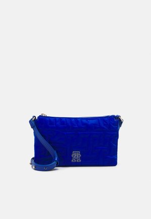 Heldere blauwe crossbodytas met een gegraveerd geometrisch patroon, gouden "TH"-logo aan de voorkant en verstelbare riem met metalen gesp.
