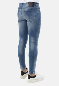 Blauwe skinny jeans met een vervaagde was, vijf zakken en een zwart logo label op de tailleband, gecombineerd met witte sneakers met zwarte accenten.
