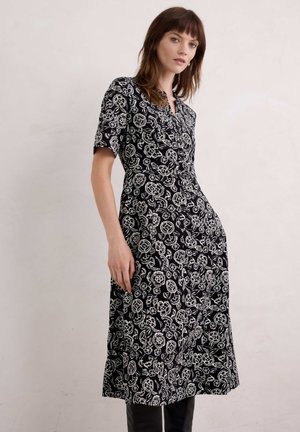 Schwarz-blumiges Kleid mit kurzen Ärmeln, V-Ausschnitt und A-Linie. Verfügt über weiße Blumenmuster und einen Knopfverschluss vorne.