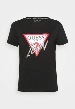 Black cotton t-shirt with short sleeves, featuring a red triangular logo "GUESS" and "ICON" printed in sparkling silver letters.