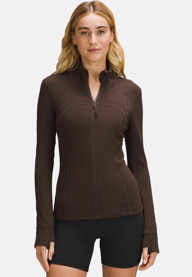 Brown zip-up athletic jacket with long sleeves and thumbholes, featuring seam accents and two zippered pockets on the front.