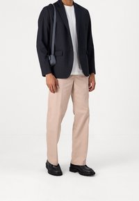 Maßgeschneiderter Marineblazer mit Nadelstreifen, weißes T-Shirt, beige Hose und schwarze klobige Stiefel. Enthält eine kleine Umhängetasche mit Riemen.