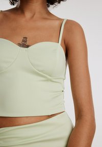 Lichtgroene cropped top met dunne bandjes, textuurstof en een sweetheart halslijn. Opvallende naaddetails bij de buste.