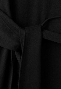 Zwart gebreide stof met een detail van een gestrikte riem. De textuur is zacht en de stof heeft een gladde, egale afwerking.