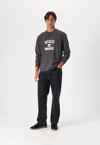Camisa de manga larga gris con el texto blanco "DICKIES 817 WORKWEAR", combinada con jeans negros y zapatillas negras con suelas de goma. Diseño sencillo.