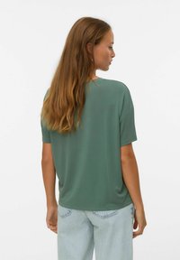 Groene T-shirt met korte mouwen en een ontspannen pasvorm, gemaakt van een soepele stof. Gecombineerd met lichtblauwe spijkerbroek, gezien vanaf de achterkant.