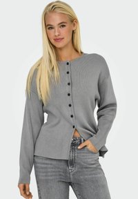 Grå knapprad cardigan i ribbad textur med långa ärmar, accentuerad med svarta knappar och en avslappnad passform, i kombination med grå jeans.