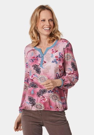 Rosa Bluse mit floralen und Paisleymustern, V-Ausschnitt und blauen Akzenten am Kragen und an den Manschetten. Lange Ärmel mit elastischen Bändern.