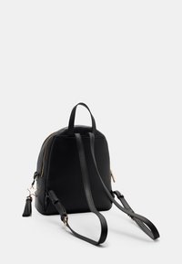 Schwarzer Kunstleder-Rucksack mit runder Form, verstellbaren Trägern, goldfarbenen hardware Akzenten und einem Quasten-Detail. Reißverschlussverschluss oben.