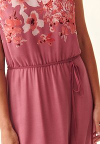 Robe florale d'une couleur rose poussiéreux, en tissu léger, avec des manches courtes, un cordon à la taille et de vives motifs floraux roses et blancs.