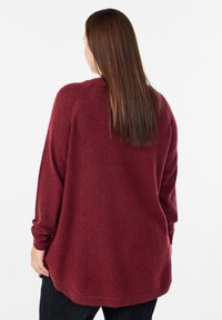 Burgundijas krāsas pārmērīgs džemperis, izgatavots no mīksta materiāla, ar noapaļotu apakšmalu un garām piedurknēm ar ribotām malām. Vienkāršs dizains bez rakstiem.