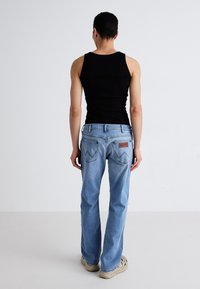 Jean en denim bleu clair avec une coupe décontractée, arborant une patch en cuir brun de la marque et deux poches arrière avec des accents de couture.