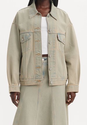 Femme portant une veste en jean beige clair sur un crop top blanc et une jupe en jean beige taille haute assortie.