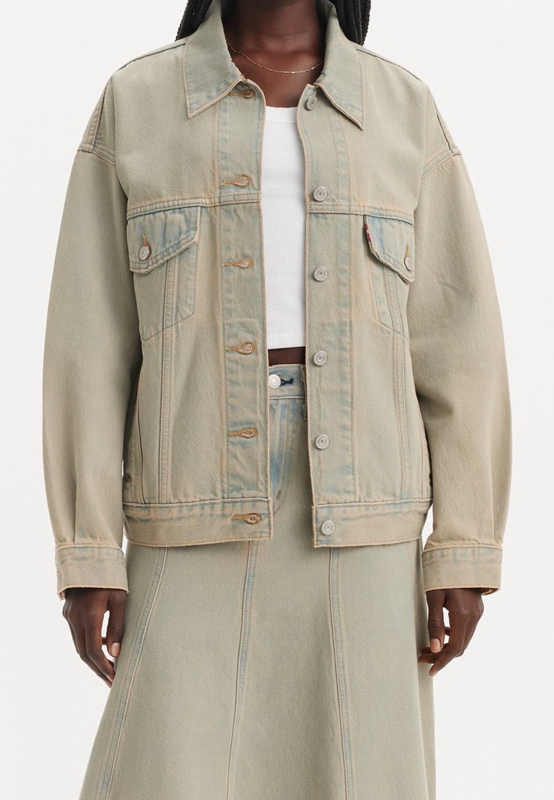 Femme portant une veste en jean beige clair sur un crop top blanc et une jupe en jean beige taille haute assortie.