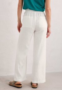 Witte linnen wijde broek met elastische tailleband, voorzien van twee achterzakken. Gekocht met een teal gekleed bovenstuk en bruine sandalen.