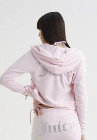 Felpa rosa con gonna abbinata e lettering in strass "Juicy". Materiale morbido, tasche anteriori e cappuccio con dettaglio a laccio sul retro.