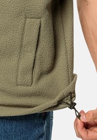Helles olivengrünes Fleece-Pullover mit strukturiertem Stoff, Seitentasche und verstellbarem Kordelzug am Saum. Nahaufnahme des Kordelzuges.