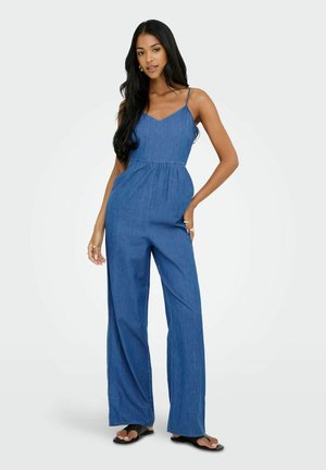 Combinaison en denim avec de fines bretelles, bustier ajusté et jambes larges. Couleur bleu uni, texture douce, avec un détail de taille smockée.