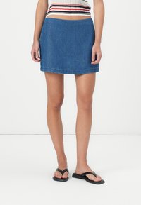 Denim mini-skjørt i mørkeblå, med en rett passform og kantet kant. Matchet med svarte flip-flops, båret over knærne.