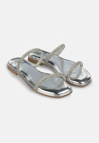 Sandali flat argento con due cinturini decorati, design a punta quadrata e finitura lucida. La suola è in materiale color marrone chiaro.