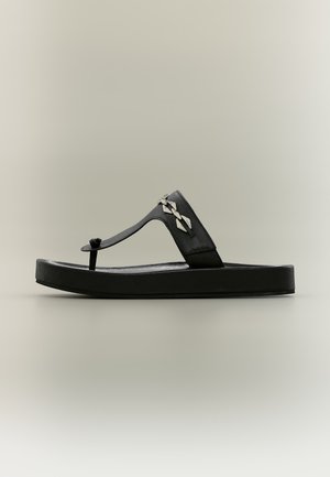 Sandale noire à plateforme de type tong, ornée d’un motif géométrique métallique sur la bride, présentée de profil sur un fond uni.