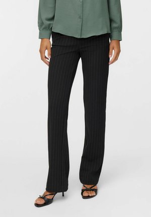 Pantalon noir à rayures, coupe ajustée, jambe droite, en tissu léger, associé à un blouse verte et des talons noirs à lanières.