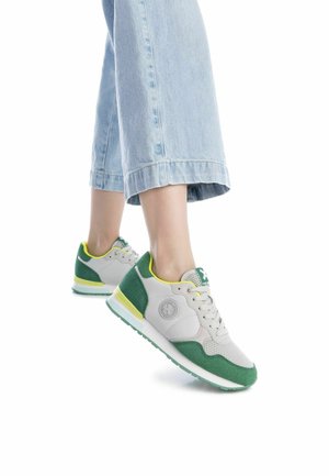 Zapatillas atléticas en gris y verde con materiales de malla y ante, que presentan un acento amarillo y un logo, combinadas con unos jeans de pierna ancha en azul claro.