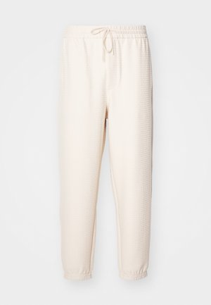 Kreemikaalsete sportlike pükstega, millel on tekstuur, elastne vöökoht, millel on nöör, ja ribatud pahkluud.