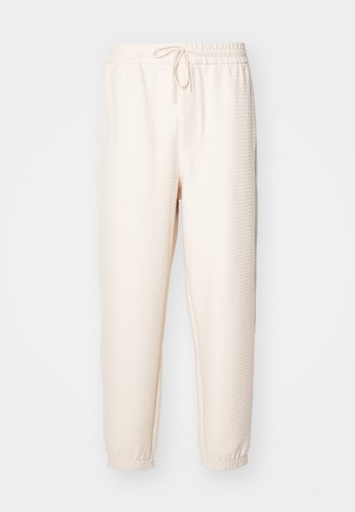 Krēmkrāsas sporta bikses ar teksturētu rakstu, elastīga josta ar aukliņu un ribota apakšmalām pie potītēm.