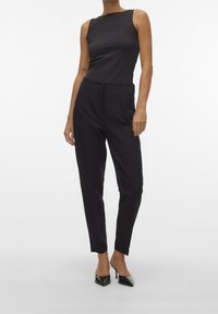 Svart ärmlös topp kombinerad med åtsittande svarta byxor. Outfiten har en slät textur, skräddarsydd design och kompletteras av spetsiga svarta klackar.