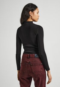 Fekete, hosszú ujjú, bordázott felső, amely szűkített derekú, bordó farmernadrággal van párosítva, bőrcímkével és hátsó zsebekkel.