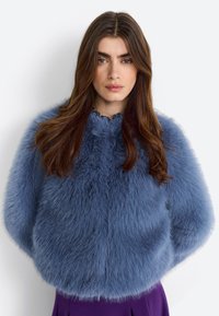 Faux fur jacket in light blue with a fluffy texture, rounded shoulders, and a scalloped neckline, worn over a purple skirt.