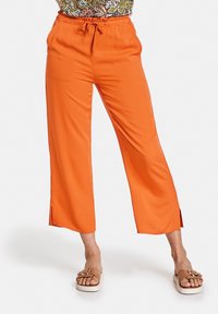 Pantalon large orange avec cordon de serrage à la taille, présentant des fentes latérales au bas pour faciliter les mouvements et une texture lisse et légère.