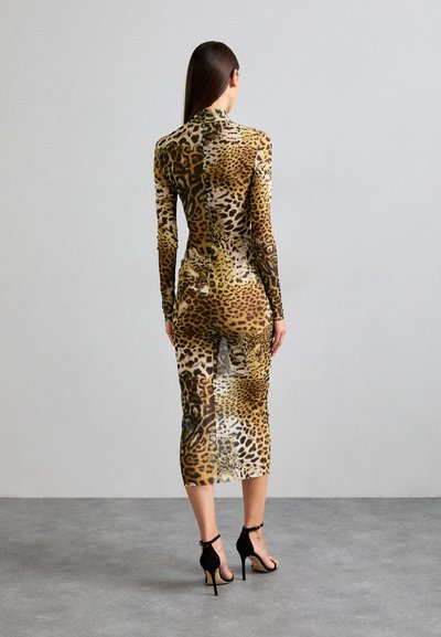 Long, form-fitting dress made from stretchy fabric featuring a multicolored leopard print. High neckline and long sleeves. Black heels.