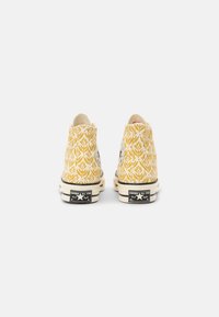 Paire de baskets montantes Converse All Star jaunes et blanches à motif, vues de dos sur fond blanc uni.