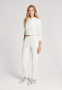 Skrojona biała bluza z kapturem z kieszonkami z przodu, w połączeniu z białymi joggerami z zamkami błyskawicznymi po bokach i ściągaczami na mankietach.