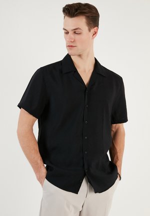 Camisa negra de manga corta hecha de un tejido ligero, con cuello de muesca y cierre delantero con botones, con un corte relajado y textura suave.
