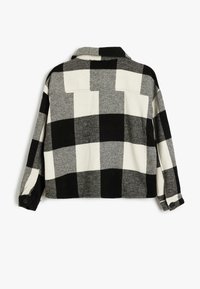 Zwart-wit geblokte flanellen shirt, met een kraag en knoppen aan de manchetten. De stof is zacht met een gestructureerde afwerking.