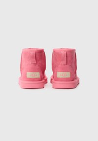 Bottines en suede rose avec une texture lisse, une forme arrondie et des semelles en caoutchouc plates. Présente un patch logo à l'arrière et un design cousu.