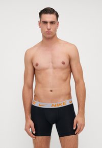 Melni bokseršorti, izgatavoti no elastīga materiāla, ar pelēku jostu, kurā ir oranžs Nike logo. Paredzēti lieliskai pieguļai.