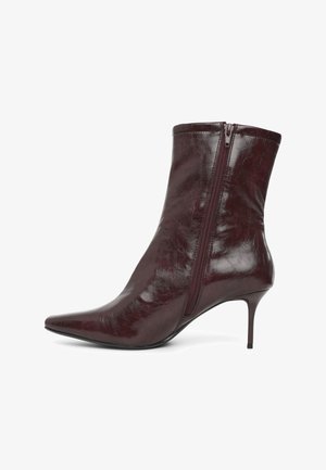 Glänzender dunkelbrauner Lederstiefelette mit spitzer Zehe, seitlichem Reißverschluss und dünnem hohem Absatz auf weißem Hintergrund.