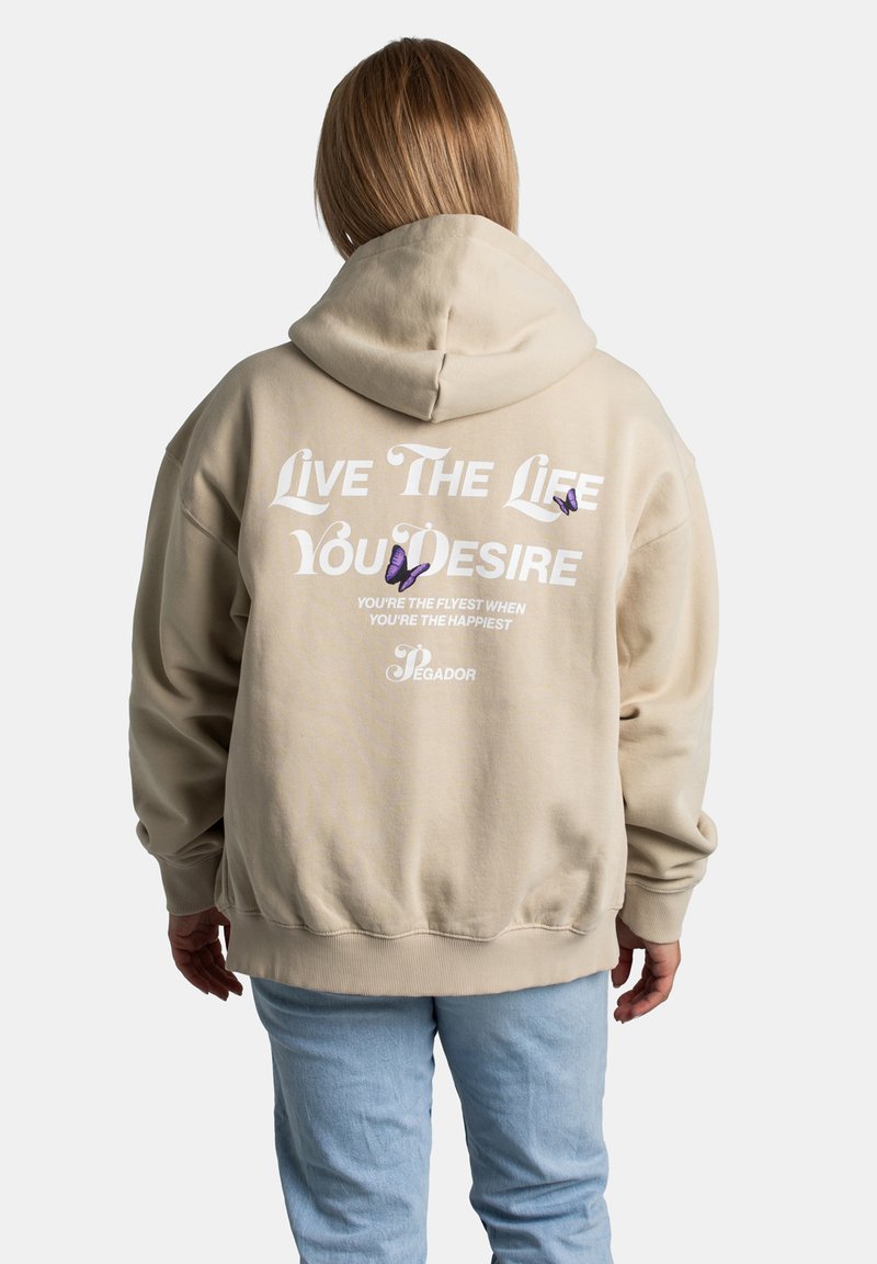 Sudadera beige con un gran gráfico en texto blanco y morado en la parte trasera. Cuenta con capucha con cordón y puños y dobladillo de canalé.