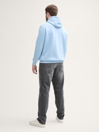 Lichtblauwe hoodie van zachte stof met een trekkoordkap, gecombineerd met vervaagde grijze jeans en witte sneakers. Gericht op een casual pasvorm en comfort.