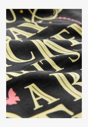 Čierna látka s vyvýšeným žltým písmom a ružovým motýlikom. Textúra sa zdá byť rebrovaná, čo zdôrazňuje detaily potlače.