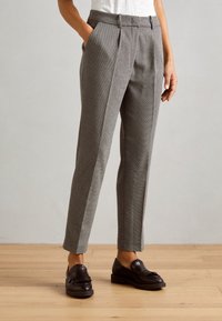 Pantalon gris à motif, coupe ajustée, avec deux poches avant, devant plat et texture lisse. Associé à des mocassins noirs.