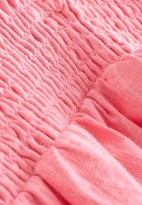 Rosa tyg med strukturerad, veckad design. Materialet verkar mjukt och lätt, med subtila variationer i nyans och djup.