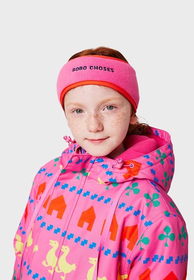 Różowa opaska z polaru z kontrastowym pomarańczowym wykończeniem i napisem "BOBO CHOSES". Modelka nosi kolorowy, wzorzysty różowy kurtkę z motywem kaczek i domów.