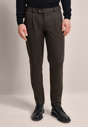 Braune, gemusterte, schlanke Chino-Hosen mit einem flachen Vorderteil, ausgestattet mit einem Knopfverschluss und Gürtelschlaufen, kombiniert mit schwarzen Dressschuhen.