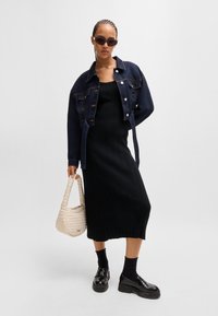 Denim jacket, black ribbed dress, braided hairstyle, black sunglasses, textured cream bag, chunky black shoes, and black crew socks.